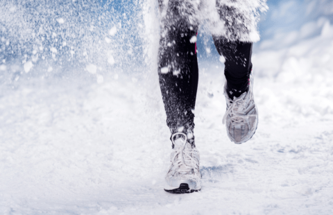 Juoksija lenkkarit jalassa lumisella tiellä.