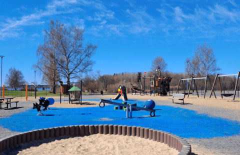 Leikkipuiston hiekkalaatikko, kiikkuja ja muita leikkipuistolaitteita.